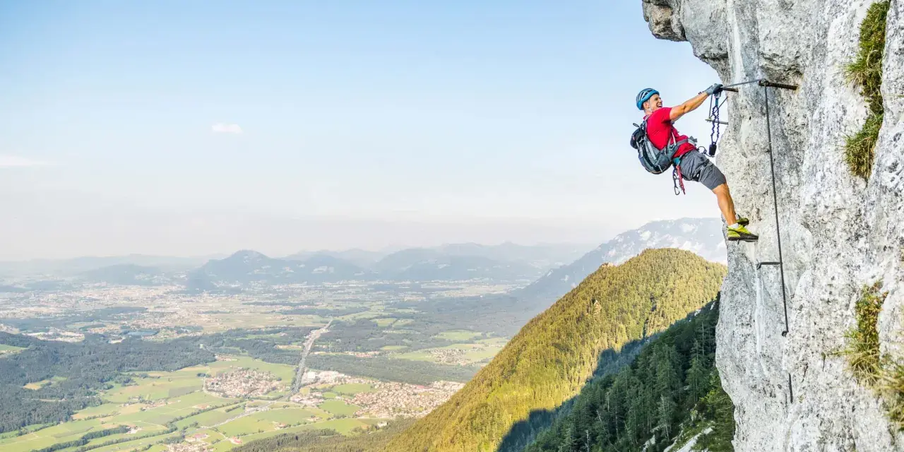 Ein Mann klettert gesichert an einem Stahlseil einen Felsgrat entlang. Ein Abenteuer auf einem der vielen Klettersteige Deutschlands.