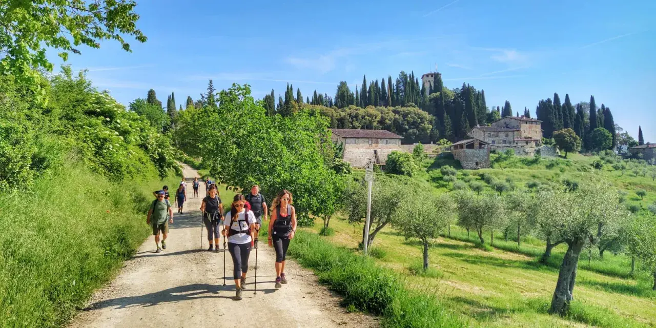 Gruppo di escursionisti su sentiero sterrato, con case coloniche e cipressi sullo sfondo. La Via degli Dei, nonostante la bellezza, presenta una certa difficoltà.