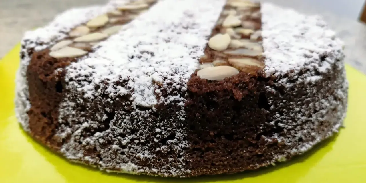 Torta caprese ricetta originale napoletana, soffice e scura, cosparsa di zucchero a velo e mandorle a lamelle.
