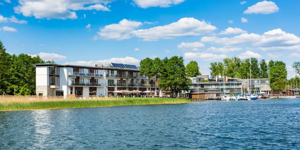 Nowoczesny Tiffi Hotel Olsztyn nad jeziorem, z łodziami przy pomoście i zielenią.