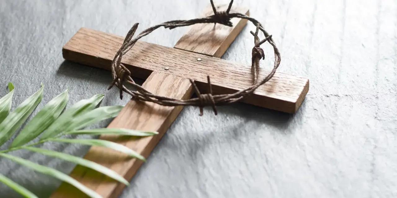 Holzkreuz mit Dornenkrone und Palmblatt. Christen fasten Regeln, um sich auf Ostern vorzubereiten.
