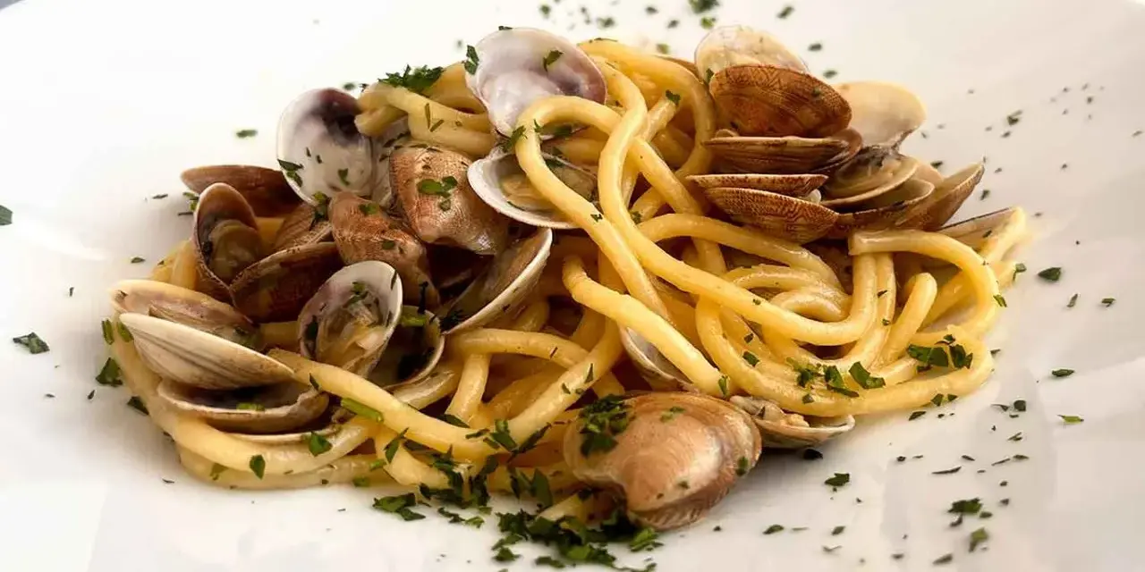 Spaghetti con lupini di mare freschi, un piatto che profuma di mare e tradizione, guarnito con prezzemolo tritato.