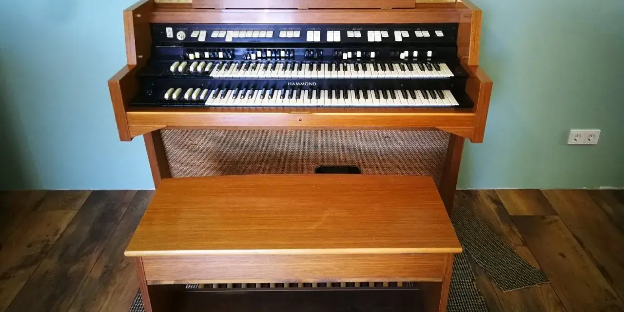 Ein schönes Hammond-Musikinstrument mit zwei Manualen und einer Holzbank davor.