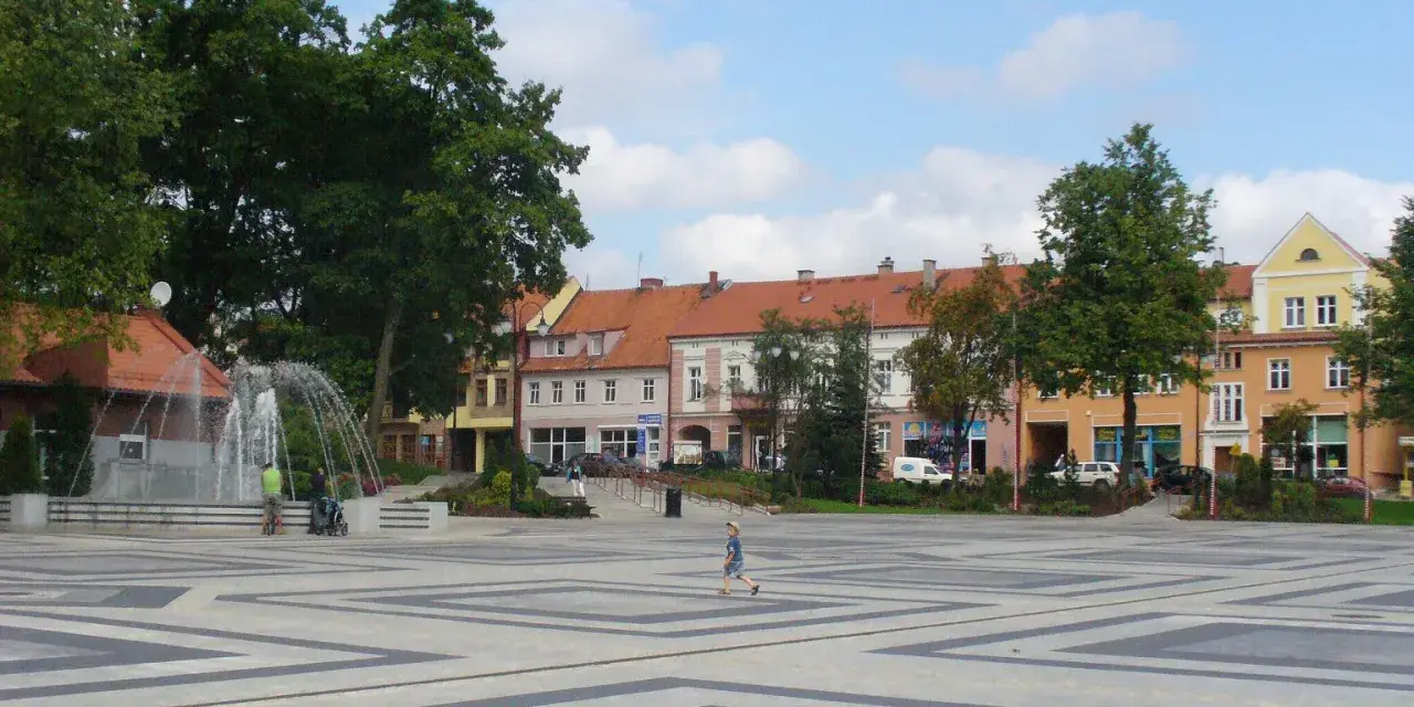 Dziecko biega po placu z fontanną, otoczonym kamienicami. To największy rynek w Polsce, tętniący życiem.