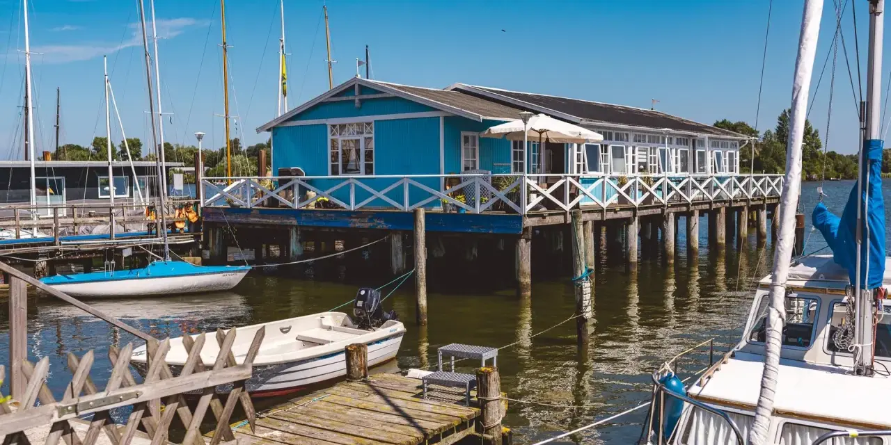 Blaues Haus am Wasser mit Booten, ein idyllisches Motiv für Schlei Ausflugsziele.