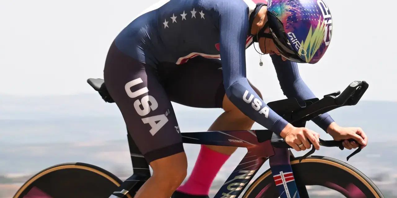 Chloé Dygert, in her USA cycling kit, races against the clock, her focus intense as she powers her bike uphill.