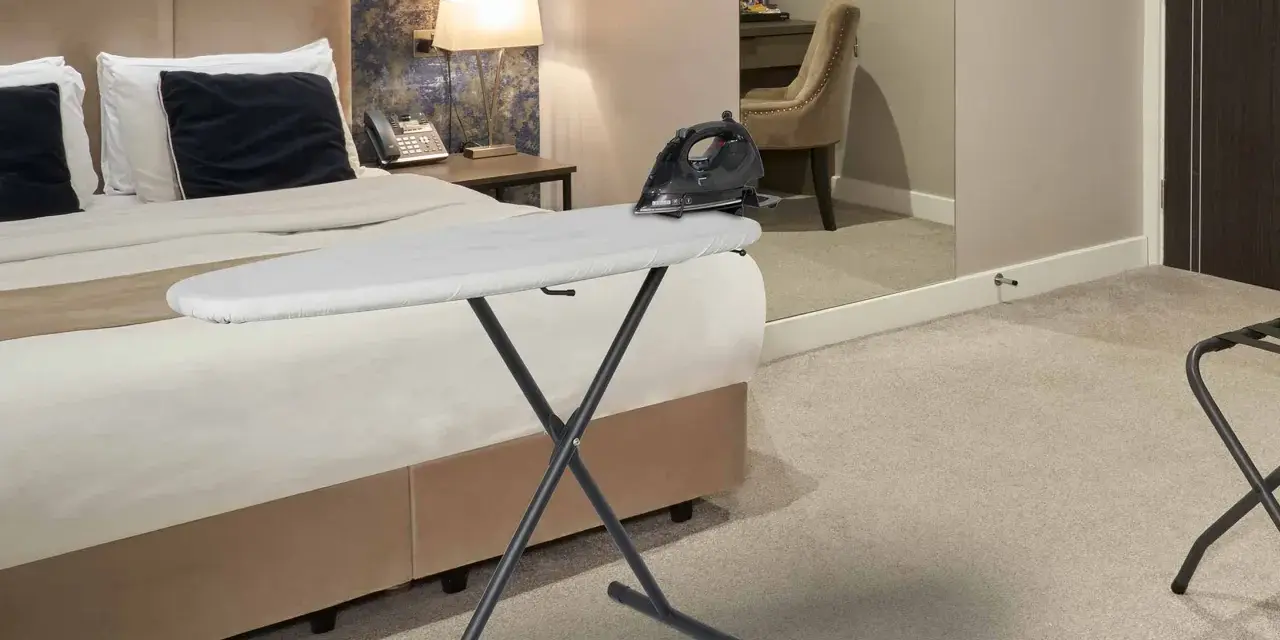 Deska do prasowania z żelazkiem na łóżku w hotelowym pokoju.