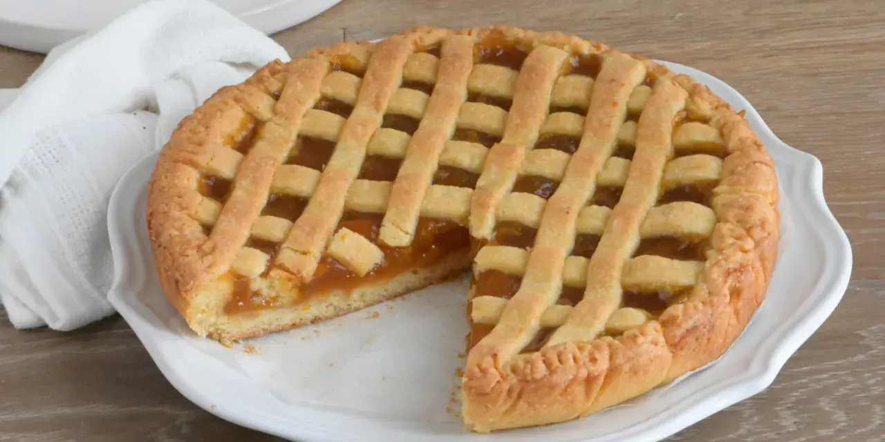 Crostata con marmellata, un classico della crostata ricetta tradizionale, servita su un piatto bianco con un tovagliolo di lino.