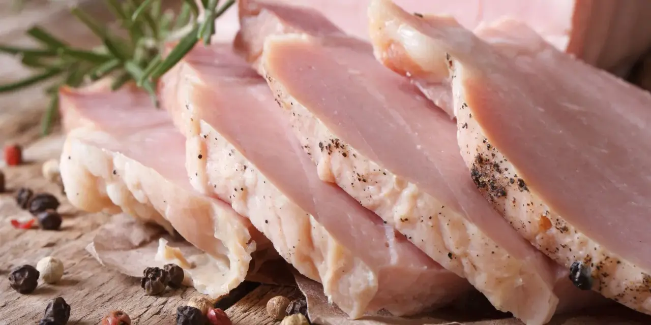 Super delikatny i soczysty schab gotowany, pokrojony w plastry, z gałązką rozmarynu i ziarnami pieprzu.