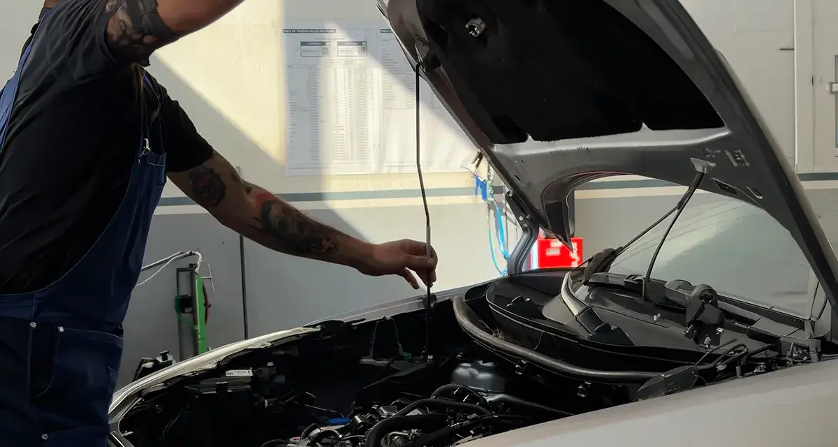 Meccanico con tatuaggi controlla il motore. Capire la differenza tra tagliando e revisione è fondamentale per la manutenzione dell'auto.
