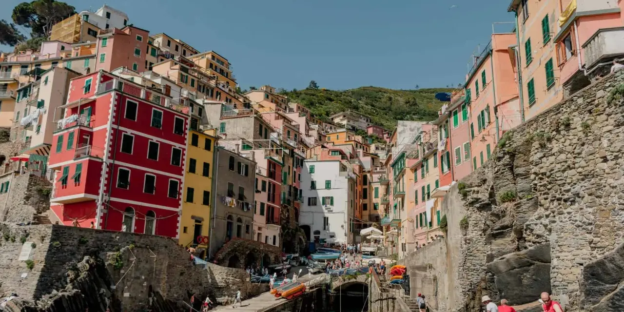 Colorful buildings cling to a hillside overlooking a harbor, a picturesque scene after a train from Bologna to Cinque Terre.
