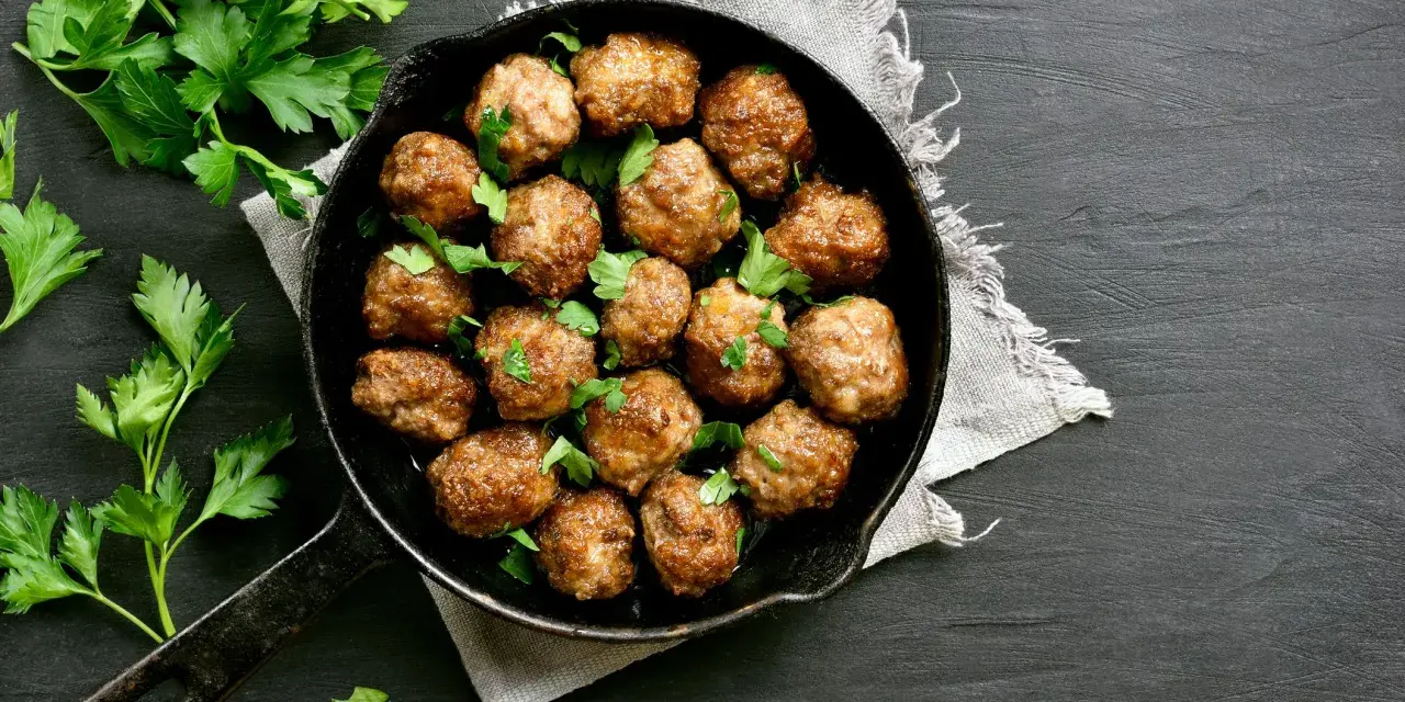 Polpette al forno dorate e succulente, guarnite con prezzemolo fresco, in una padella di ghisa su sfondo scuro.
