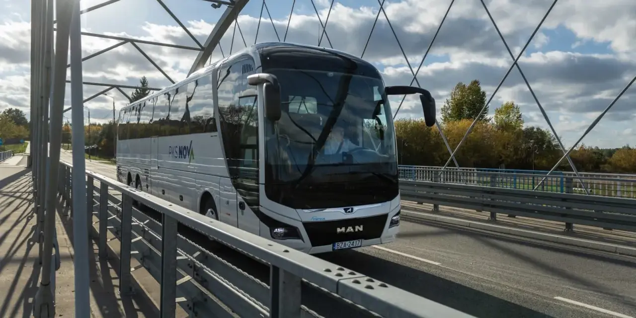 Biały autokar PKS NOVA jedzie przez most, pokonując trasę Warszawa-Augustów.