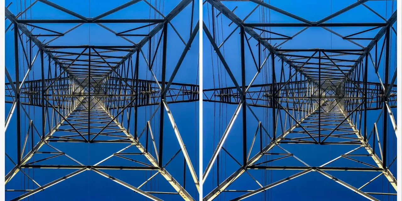 Widok z dołu na kratownicę słupa energetycznego, tworzącą geometryczny wzór na tle błękitnego nieba. To fotografia stereoskopowa.