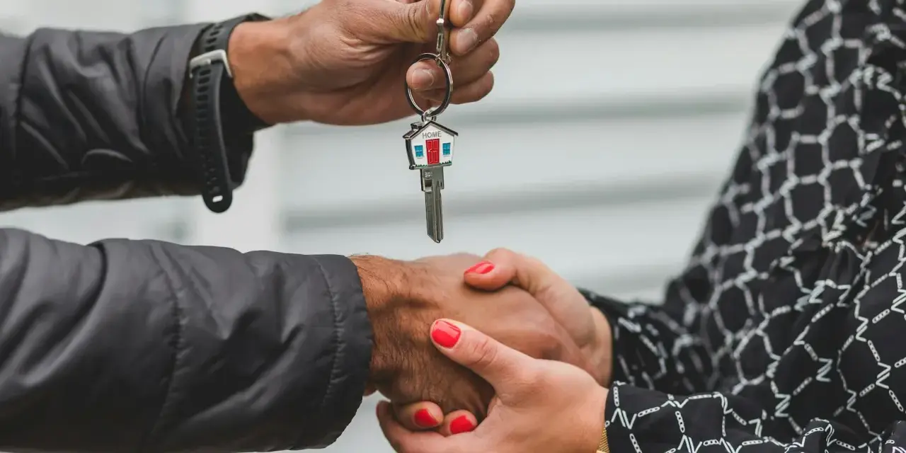 Une main tend une clé de maison, l'autre la saisit. Une poignée de main scelle un accord, peut-être une solution quand un indivisaire ne paye pas.