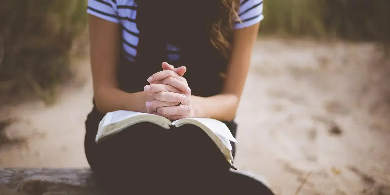 Kobieta z dłońmi złożonymi nad otwartą Biblią. To jej modlitwa o dobry dzień w pracy.