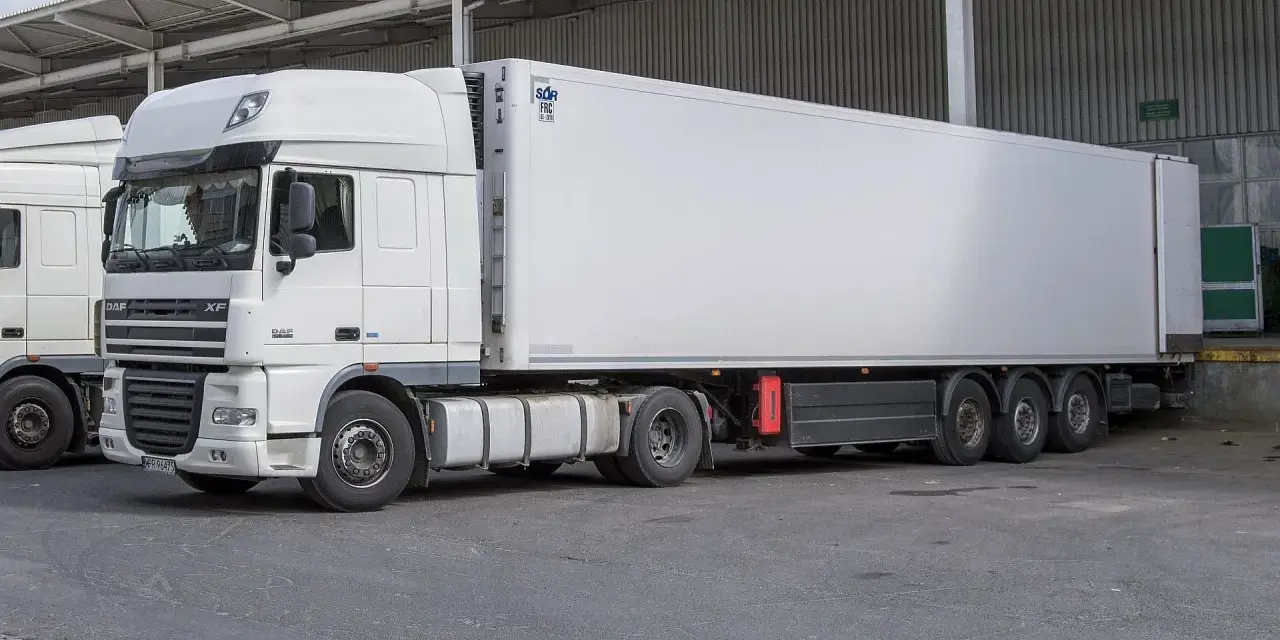 Biała naczepa DAF XF z chłodnią, gotowa do transportu. Obok stoi kolejna ciężarówka, tworząc zgrany zespół pojazdów.