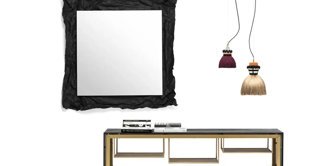 Specchio sopra madia con cornice nera stropicciata, due lampade a sospensione a forma di nappa e una madia con struttura dorata.