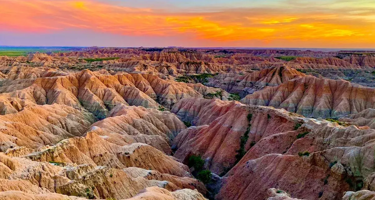 Un paisaje desértico con formaciones rocosas erosionadas, **las carcavas**, bajo un cielo anaranjado y azul al atardecer.