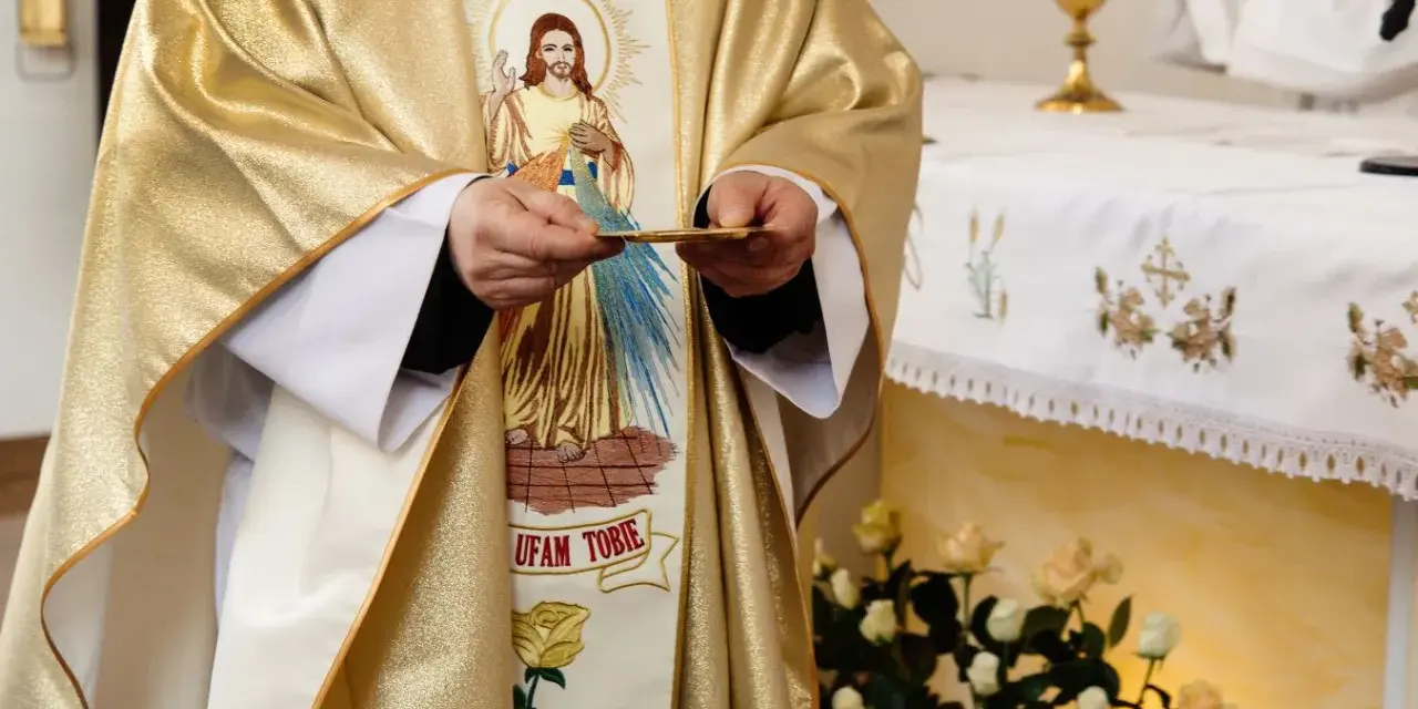 Kapłan w złotej szacie z wizerunkiem Jezusa trzyma hostię. Czy dzisiaj trzeba iść do kościoła?