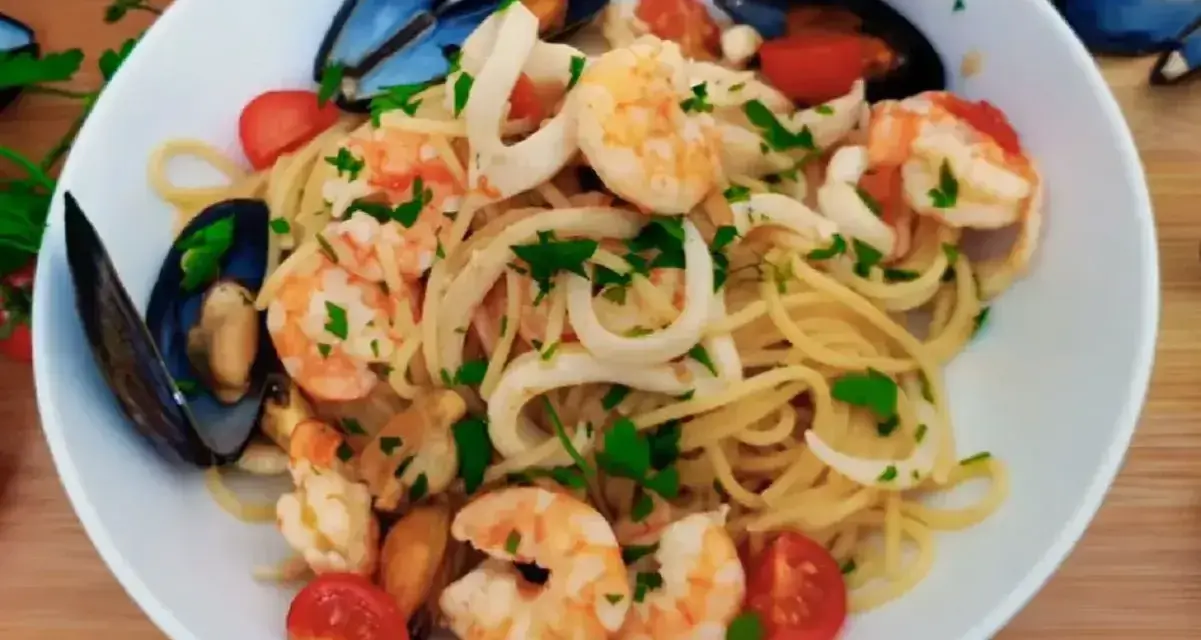 Pyszne linguini z krewetkami, kalmarami i małżami, ozdobione pomidorkami i natką pietruszki.