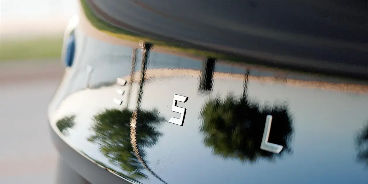 Bilens blanka lack, som en apelsinskal, reflekterar träd och himmel. Bokstäverna "ES L" syns tydligt.