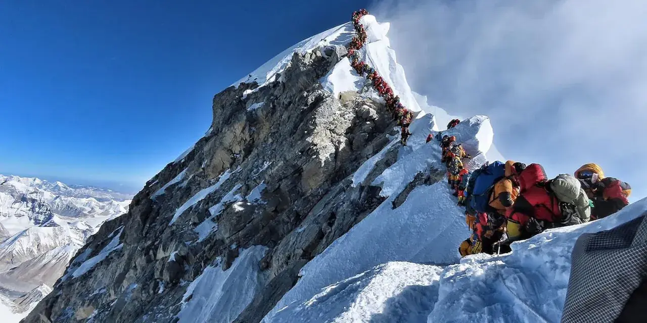 Kolejka ludzi wspinających się na najwyższą górę na świecie, Everest. Wspinacze w kolorowych kurtkach i z plecakami pokonują śnieżne zbocza.