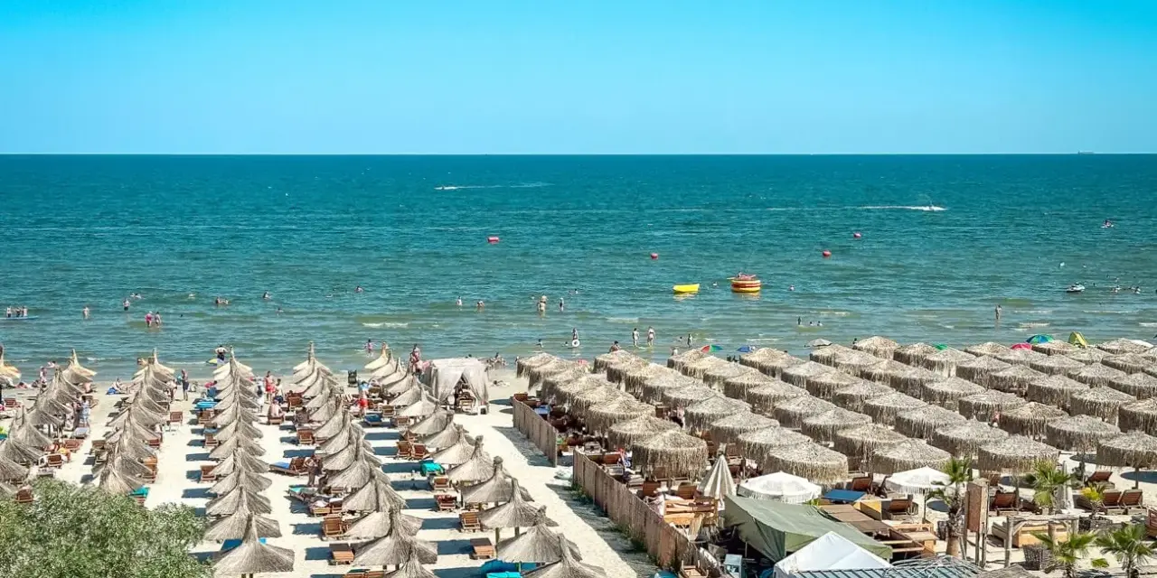 Słoneczna plaża w Rumunii, pełna leżaków i parasoli. Ludzie kąpią się w morzu, idealne miejsce na wakacje.