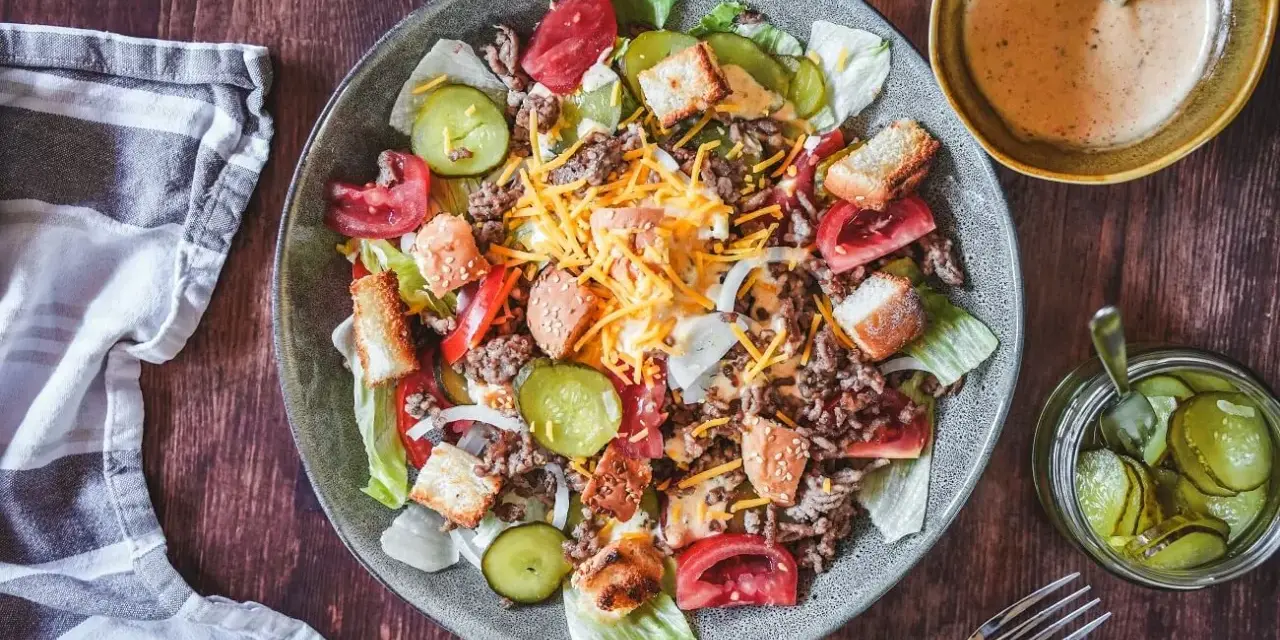 Ein Big Mac Salat mit Hackfleisch, Käse, Tomaten, Gurken und Croutons. Dazu eine cremige Sauce und eingelegte Gurken.