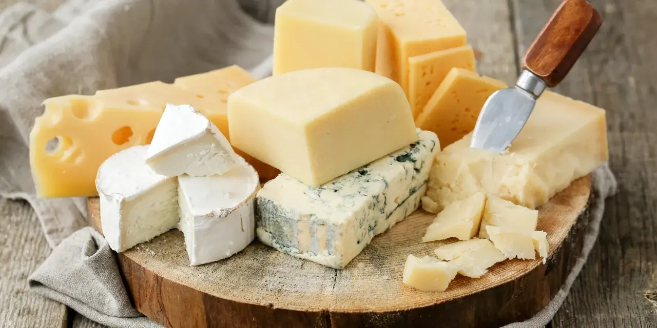 Różnorodne sery ostre gatunki: pleśniowy, żółty z dziurami, brie i parmezan, ułożone na drewnianej desce z gałązką rozmarynu.
