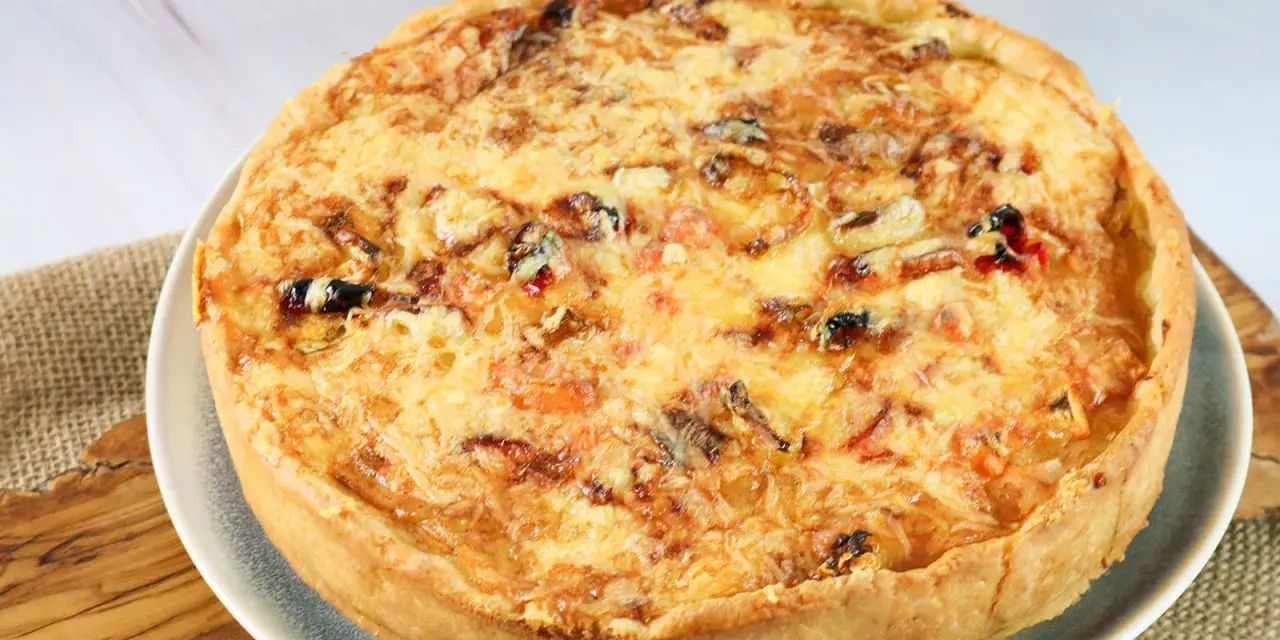 Eine goldbraune Sommer Quiche mit geschmolzenem Käse und bunten Gemüsestückchen, bereit zum Genießen.