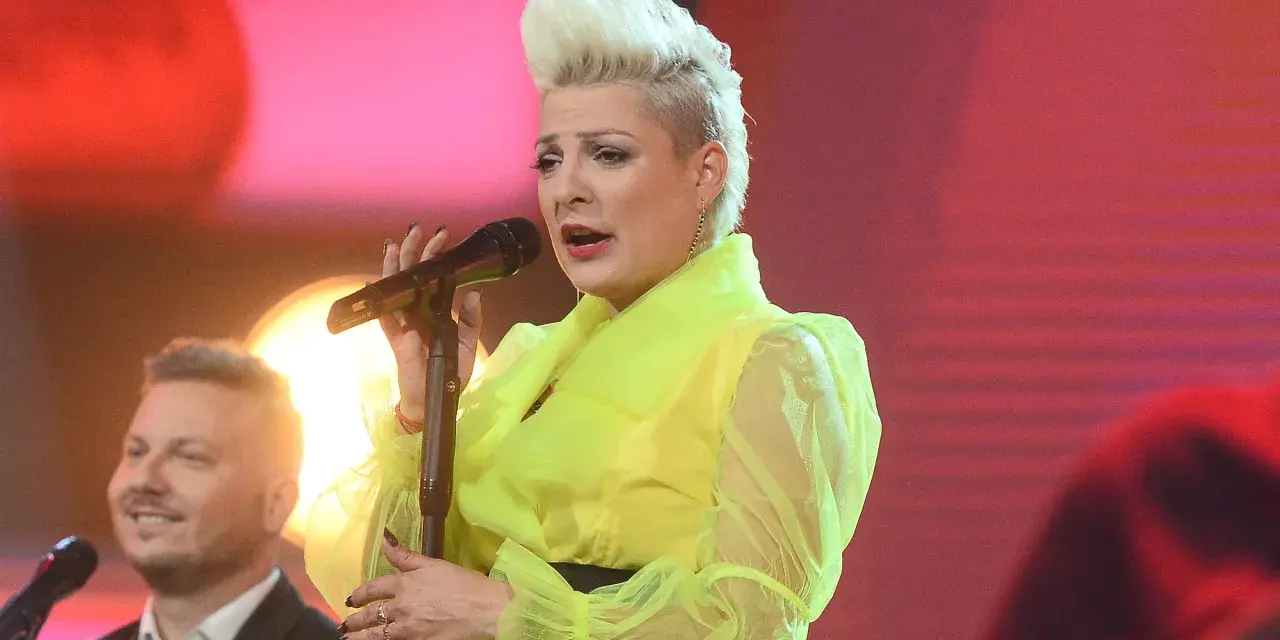 Wokalistka w neonowej kreacji śpiewa canzone d'amore, a obok niej mężczyzna z uśmiechem na twarzy.