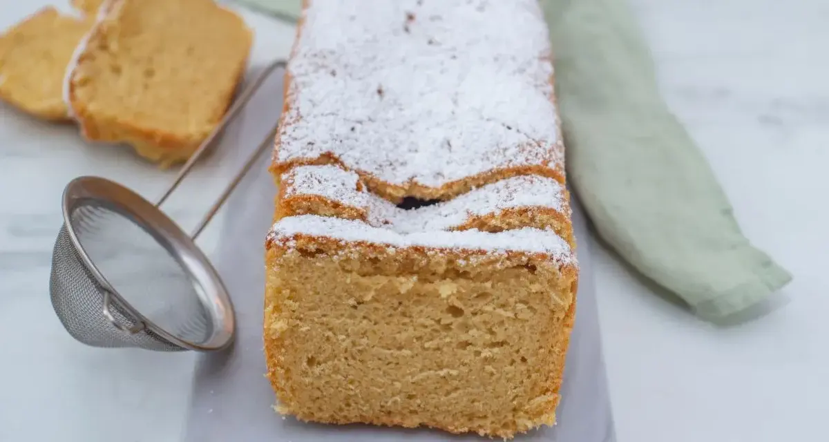 Puszyste keto ciasto z mikrofali, posypane cukrem pudrem, prezentuje się apetycznie. Obok leżą dwa kawałki ciasta i sitko.
