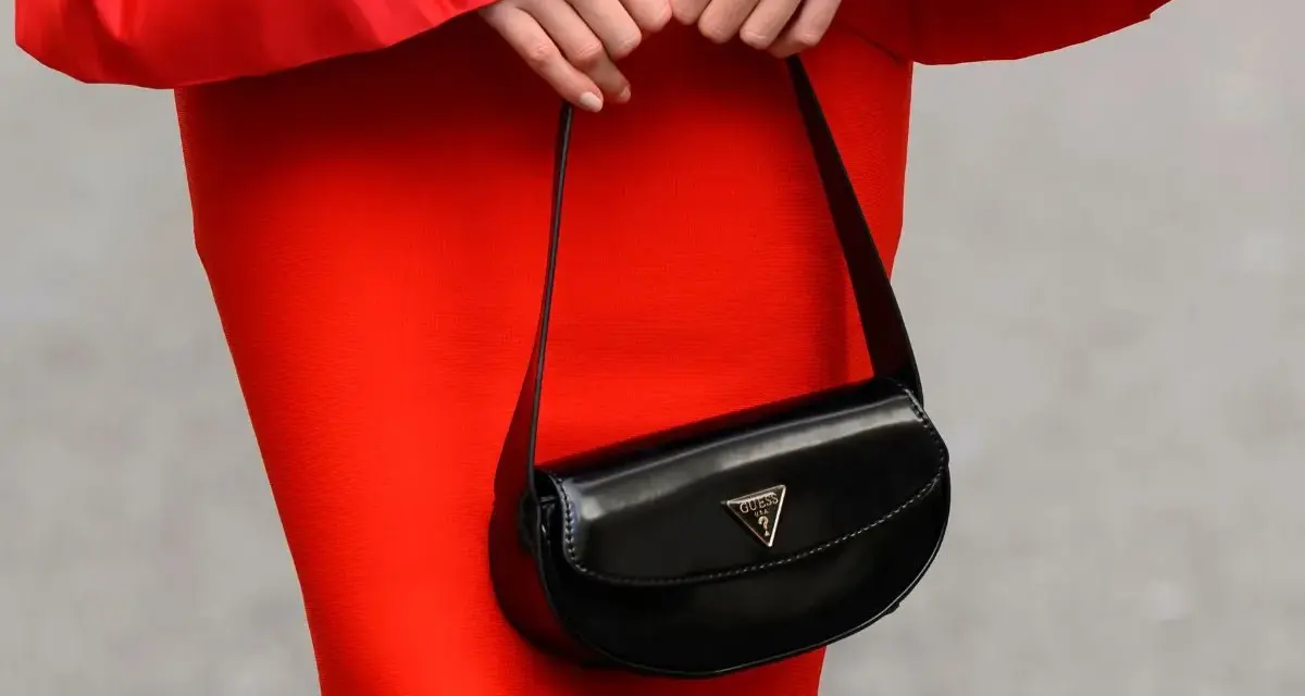 Elegancka, mała torebka Guess w kolorze czarnym, noszona do czerwonej sukienki.
