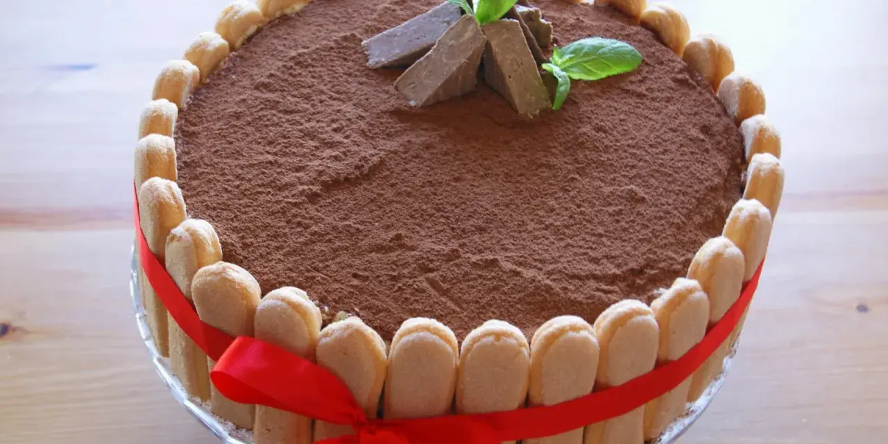 Elegancki tort whisky, udekorowany biszkoptami, kakao i miętą. Czerwona wstążka dodaje mu uroku.