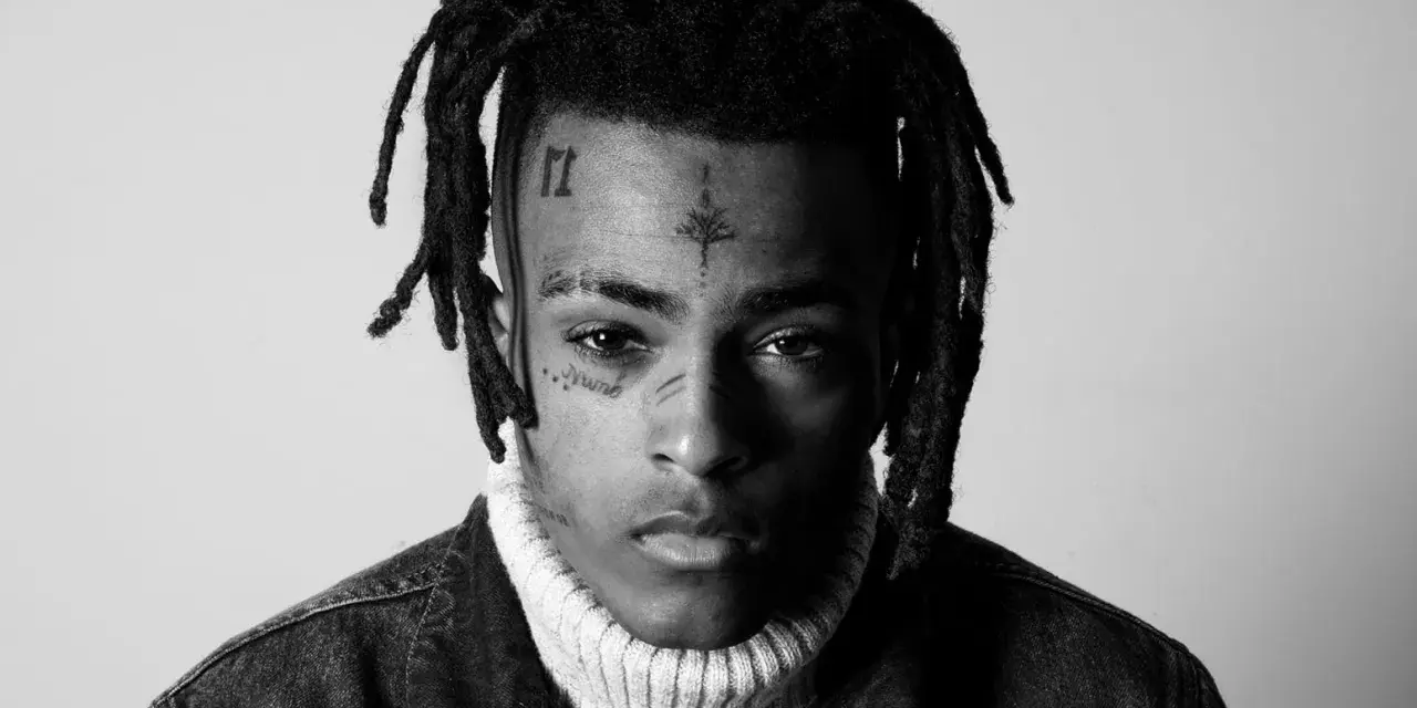 Czarno-białe zdjęcie rapera z tatuażami na twarzy, w golfie i kurtce dżinsowej. Wiele osób wspominało go, kiedy umarł xxxtentacion.
