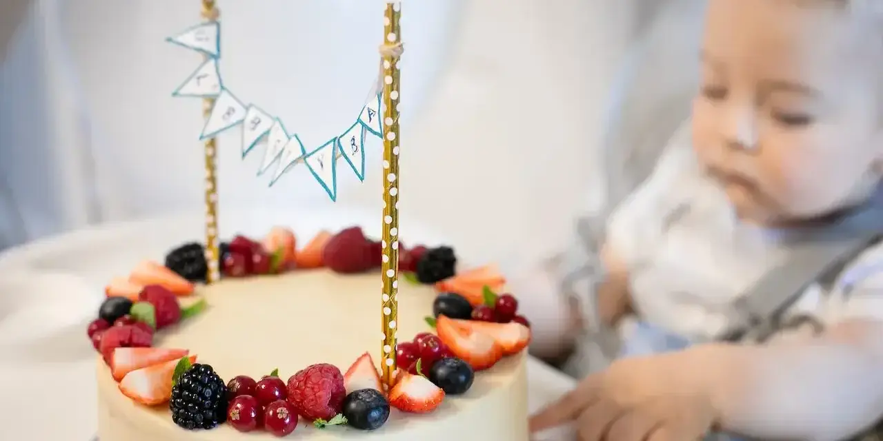 Słodki tort z owocami na przyjęcie dla dzieci. Maluch z zaciekawieniem patrzy na pyszny deser.