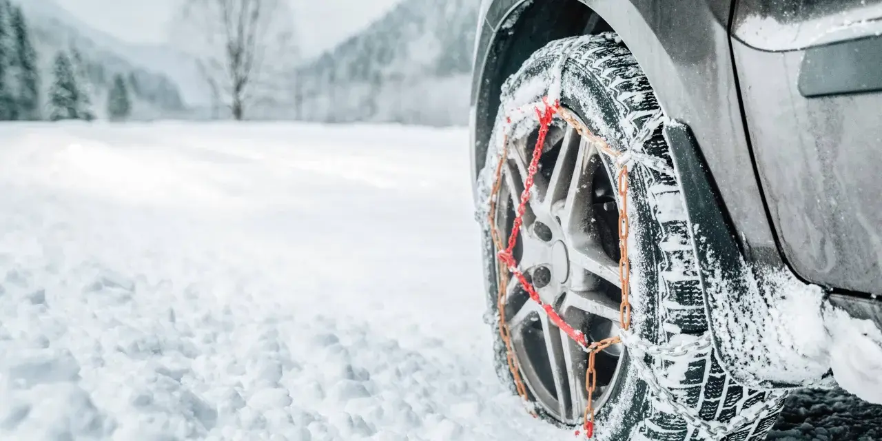 Ruota di un'auto con catene da neve su una strada innevata. Per affrontare la neve, quante catene da neve servono? Di solito due, una per ogni ruota motrice.