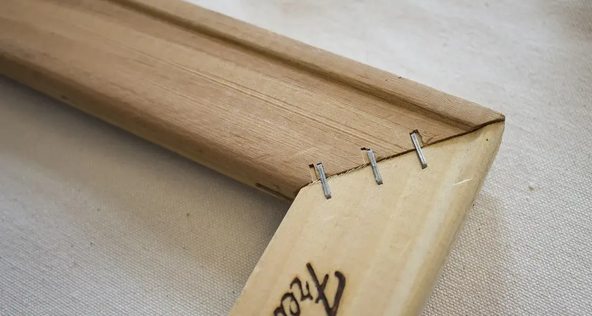 Détail d'un coin de cadre en bois, montrant comment tendre une toile sans châssis avec des agrafes.