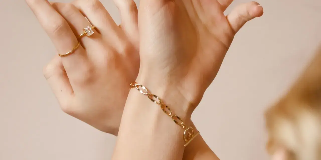 Mani adornate con anelli e un bracciale in metallo che sembra oro, un tocco di eleganza discreta.
