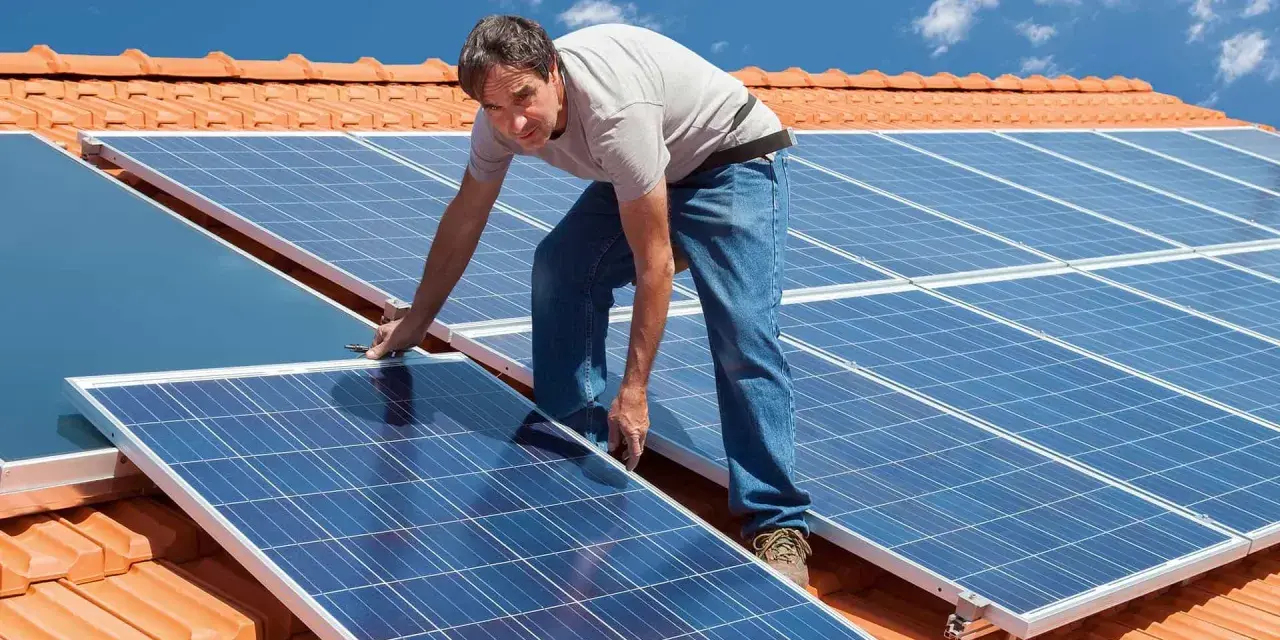 Instalator montuje panele fotowoltaiczne na dachu. Pokazuje, jak zamontować panele fotowoltaiczne, by czerpać energię ze słońca.