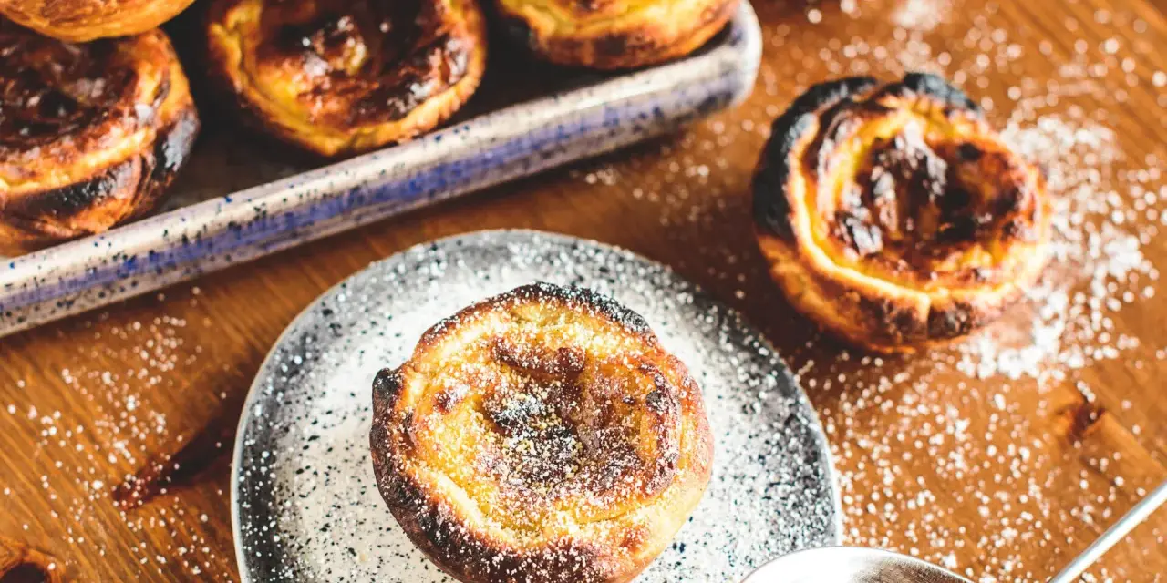 Leckeres Pastel de Nata Rezept: goldbraune Törtchen mit Puderzucker bestäubt, bereit zum Genießen.