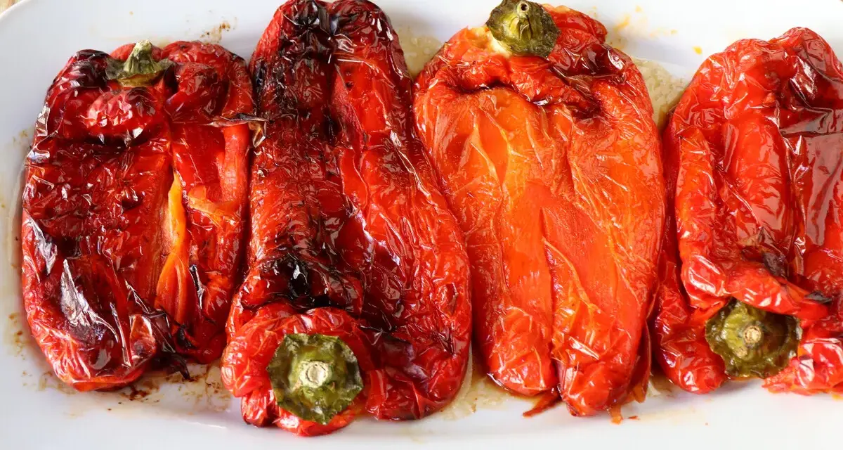 Cuatro pimientos rojos asados en freidora de aire, jugosos y con la piel ligeramente tostada, servidos en una bandeja blanca.