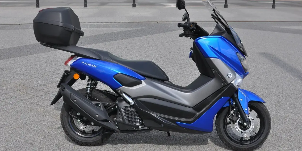 Niebieski skuter Yamaha NMAX 125 z kufrem, gotowy do jazdy. Jego prędkość maksymalna pozwoli na szybkie przemieszczanie się po mieście.