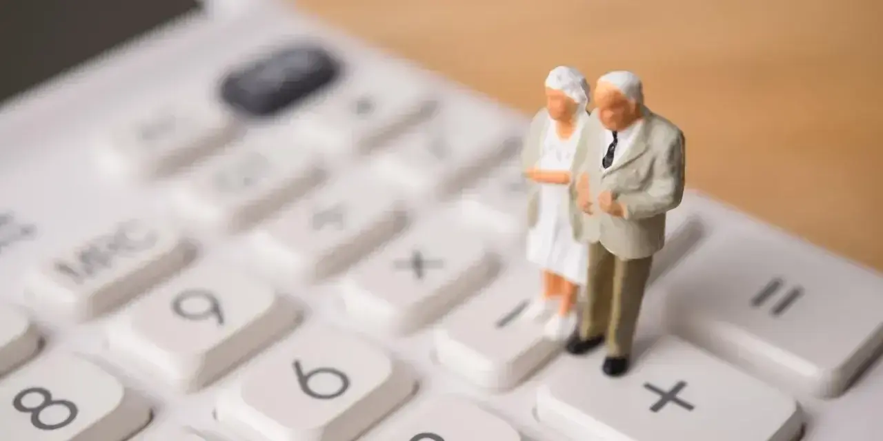 Figurki starszej pary na kalkulatorze symbolizują planowanie przyszłości i obliczanie emerytury stażowej.
