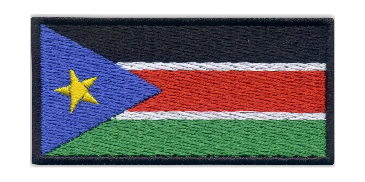 Naszywka z flagą Sudanu Południowego. Czarny pas na górze, pod nim biały, czerwony i zielony pas. Z lewej strony niebieski trójkąt z żółtą gwiazdą.