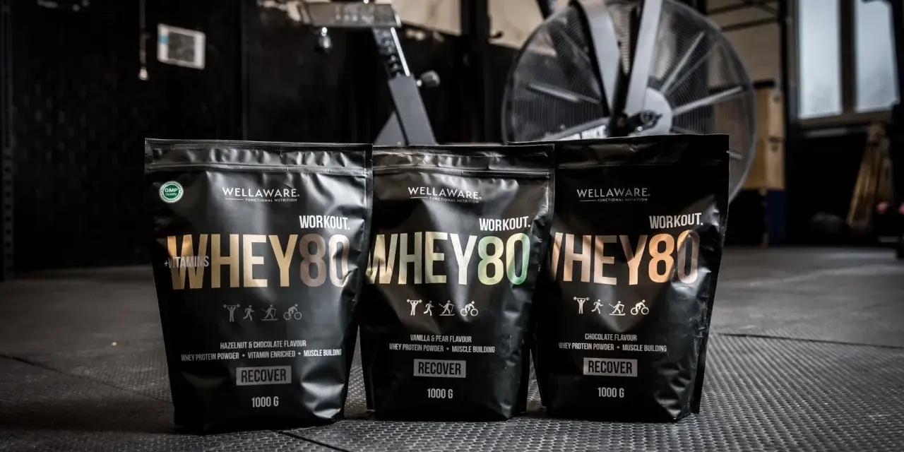 Tre påsar med Wellaware Whey80 proteinpulver står uppradade på ett gymgolv. Perfekt för återhämtning efter träning, oavsett om du föredrar vassle eller kasein.