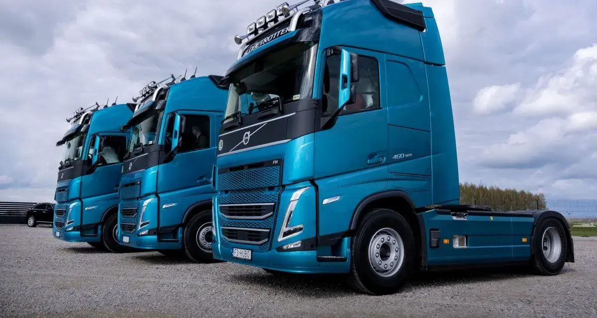 Rząd lśniących, turkusowych ciężarówek Volvo FH gotowych do transportu żywności.