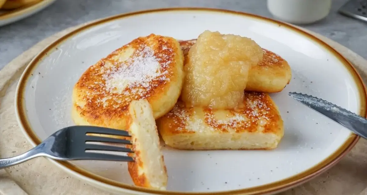 Goldbraune Quarkkeulchen, bestreut mit Zucker, serviert mit Apfelmus. Ein leckeres Quarkkeulchen Rezept zum Genießen.