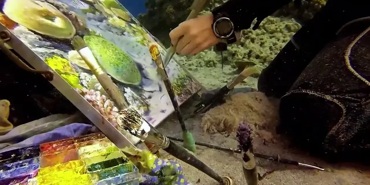 Un artiste crée une peinture sous l'eau, entouré de coraux et de poissons. Pinceaux, palette et toile sont immergés pour cette œuvre unique.